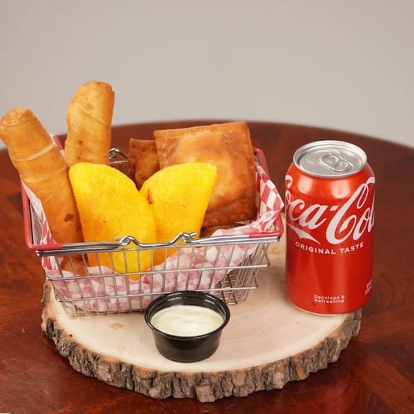 Basket of fried empanadas and taquitos with a side of sauce and a Coca-Cola can.