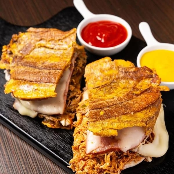Two Cuban sandwiches with shredded pork, ham, and cheese, served with ketchup and mustard.