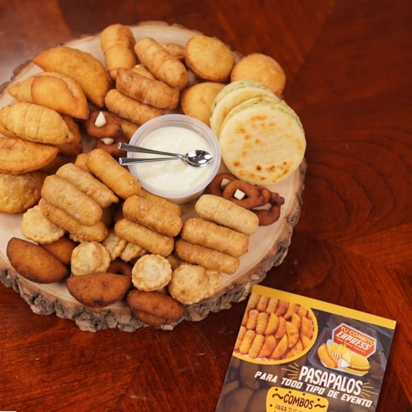 Assorted golden pastries and savory snacks surround a bowl of creamy dipping sauce on a wooden serving board.
