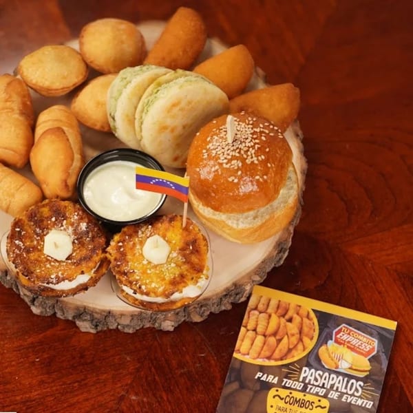 A wooden platter filled with various Venezuelan appetizers, including tequeños, empanadas, and mini arepas.