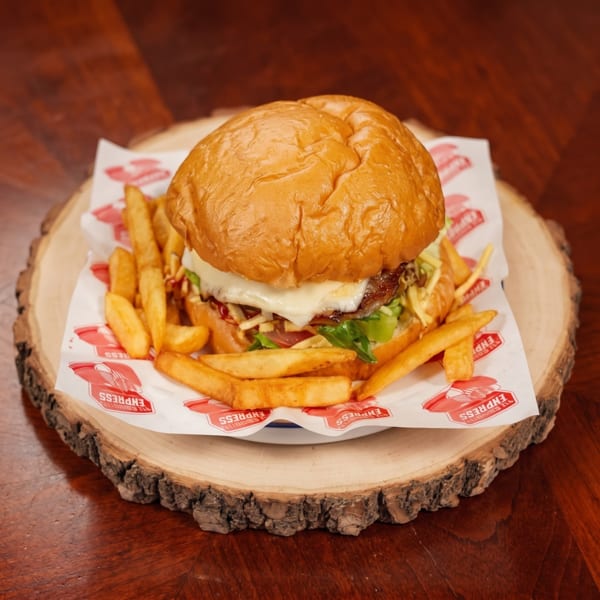 Cheeseburger with lettuce and tomato, served with golden fries on a branded paper-lined wooden platter.