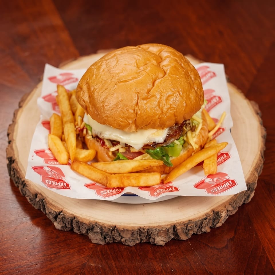 Cheeseburger with lettuce and tomato, served with golden fries on a branded paper-lined wooden platter.